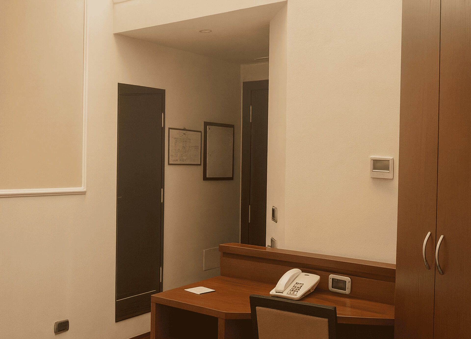Ingresso di suite junior d’hotel con scrivania in legno, sedia, telefono fisso, armadio a tutta altezza e porte interne sullo sfondo