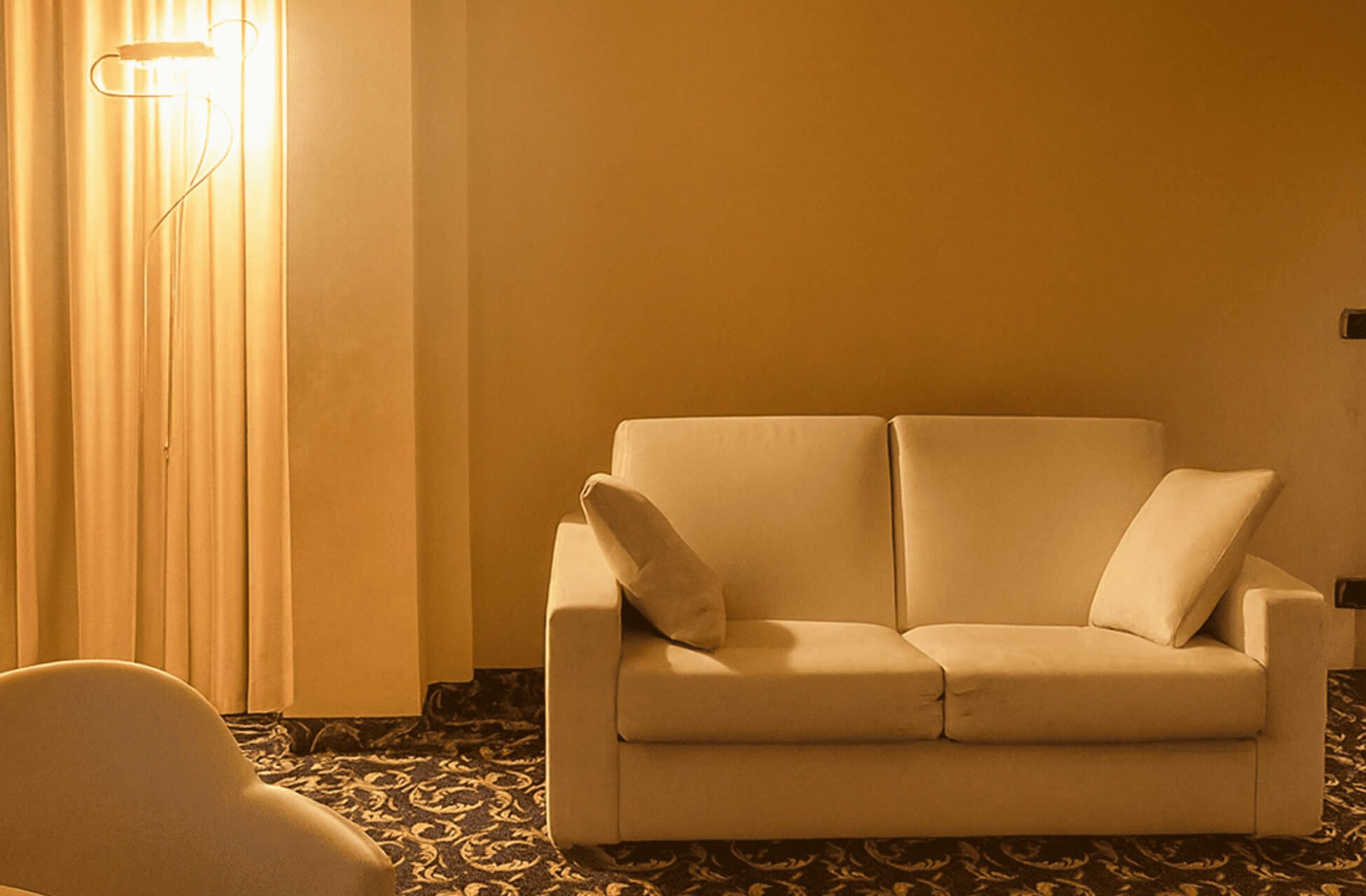 Angolo salotto con divano chiaro, lampada da terra e tende color oro.