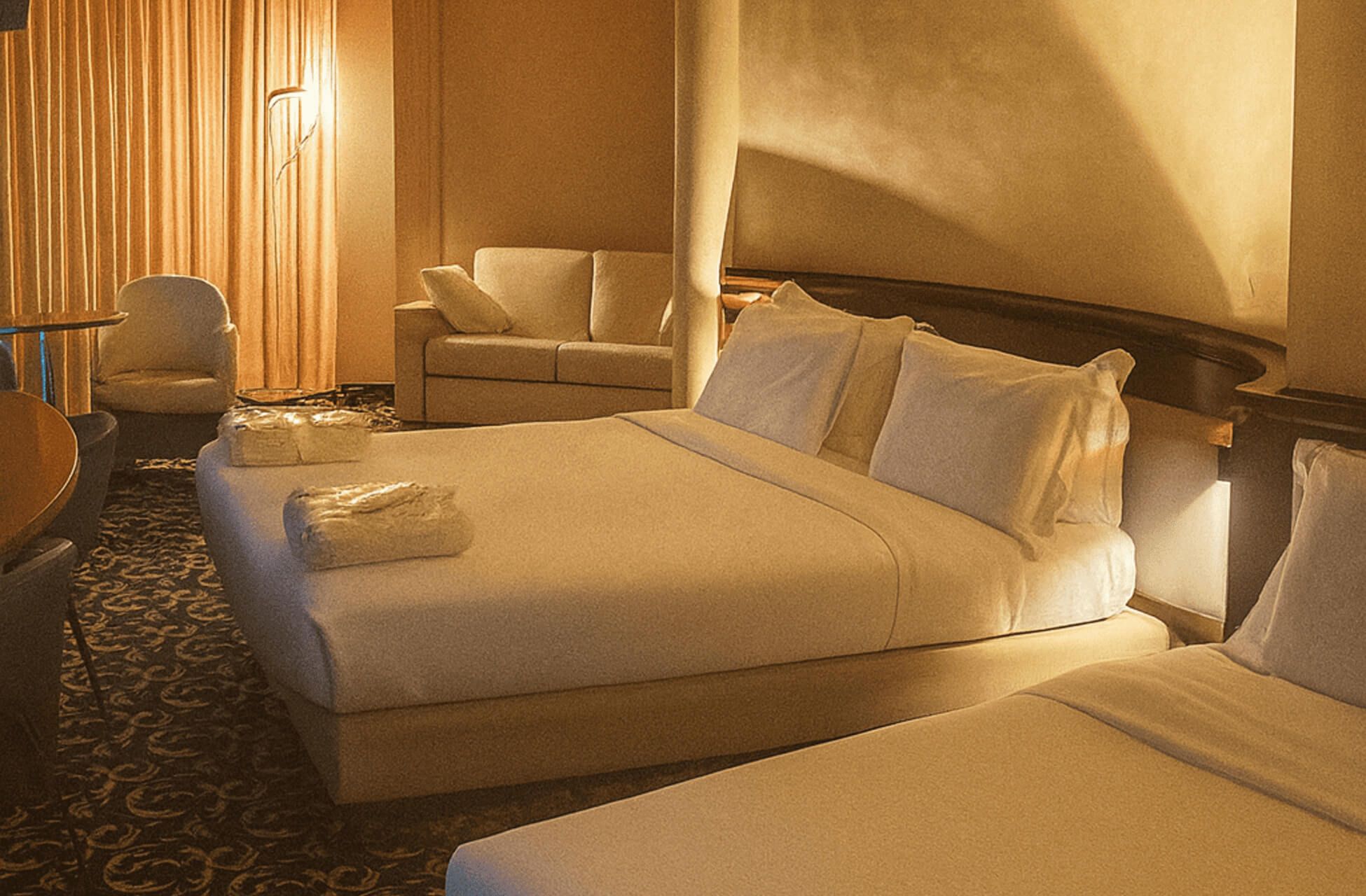 Ampia camera d’albergo con più letti, moquette decorata scura e area salotto con divano chiaro