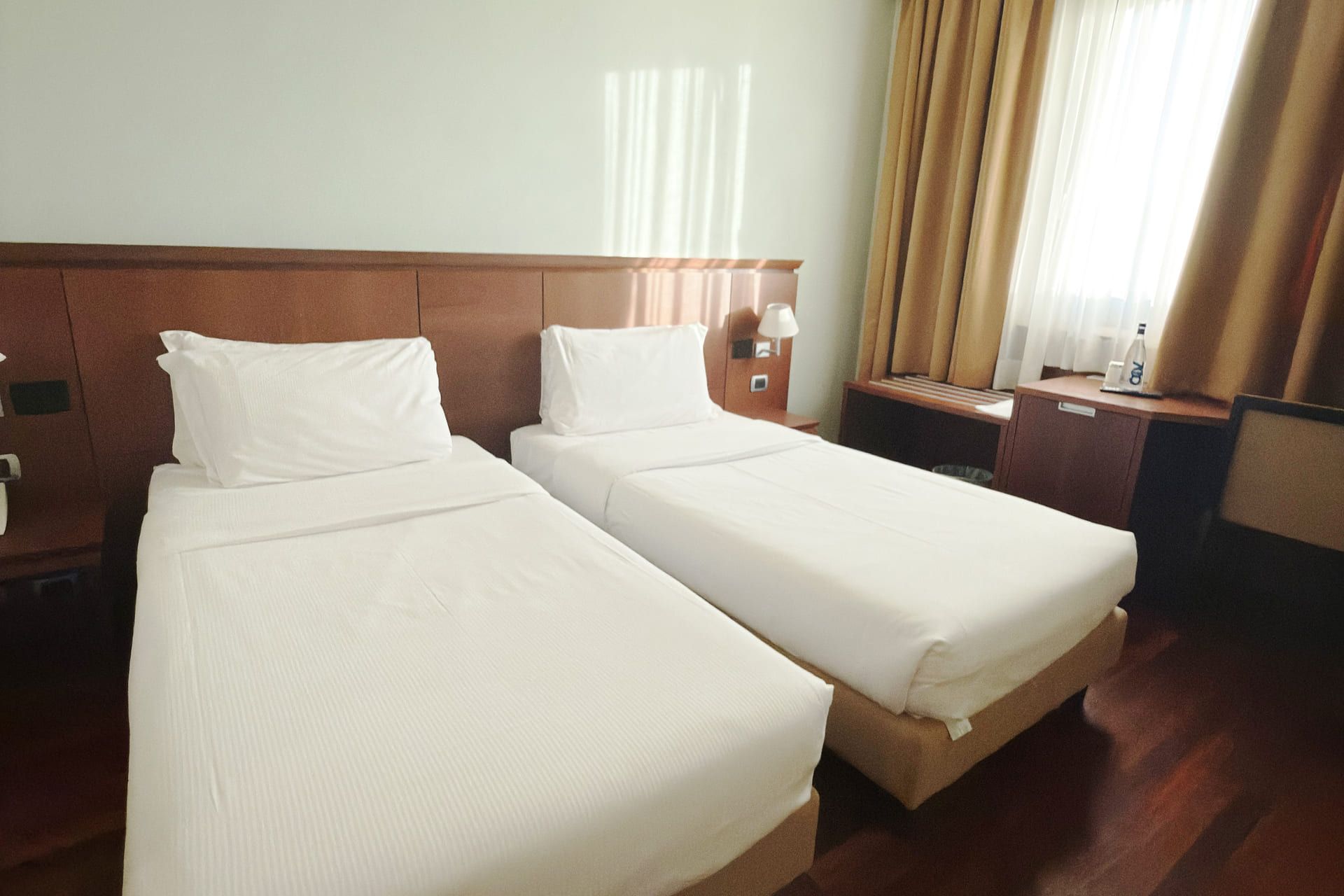 Camera d’albergo moderna con letto matrimoniale, testiera illuminata, e parete chiara 