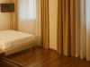Angolo di camera d’hotel con letto matrimoniale, pavimento in legno, grandi tende color ocra davanti alle finestre e TV a schermo piatto a parete.