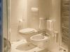 Bagno rivestito in marmo chiaro con doccia angolare, wc, bidet e scaldasalviette verticale.