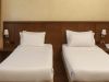 Due letti singoli affiancati di una camera tripla d’hotel, con testata in legno, comodini laterali, lampade da parete e telefono sul lato destro.