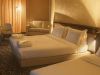 Ampia camera d’albergo con più letti, moquette decorata scura e area salotto con divano chiaro